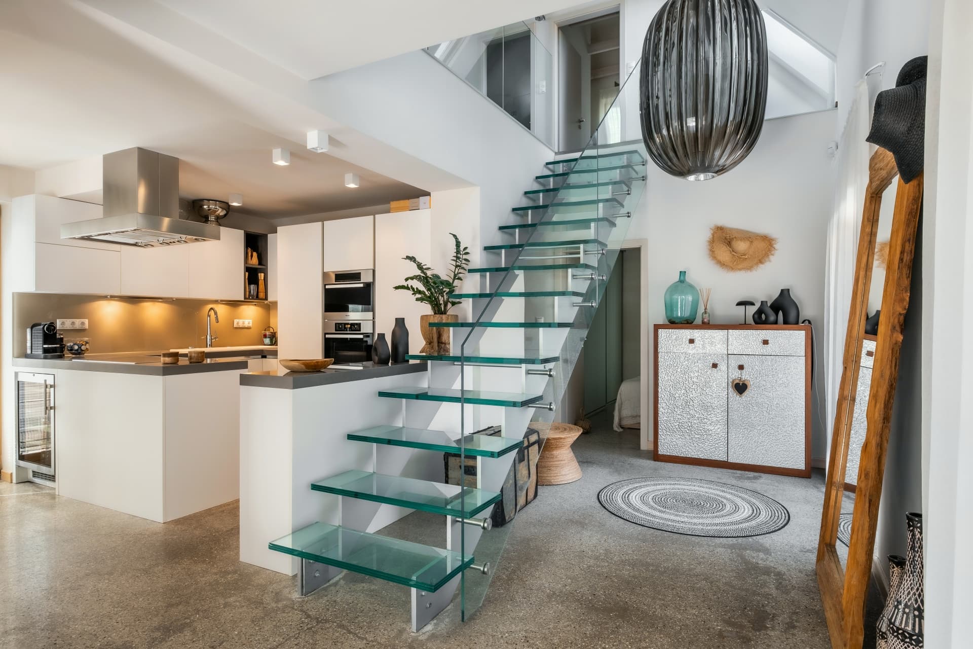 Moderne weiße Küche und Glastreppe in einem hellen, offen gestalteten Wohnraum mit stilvoller Dekoration.