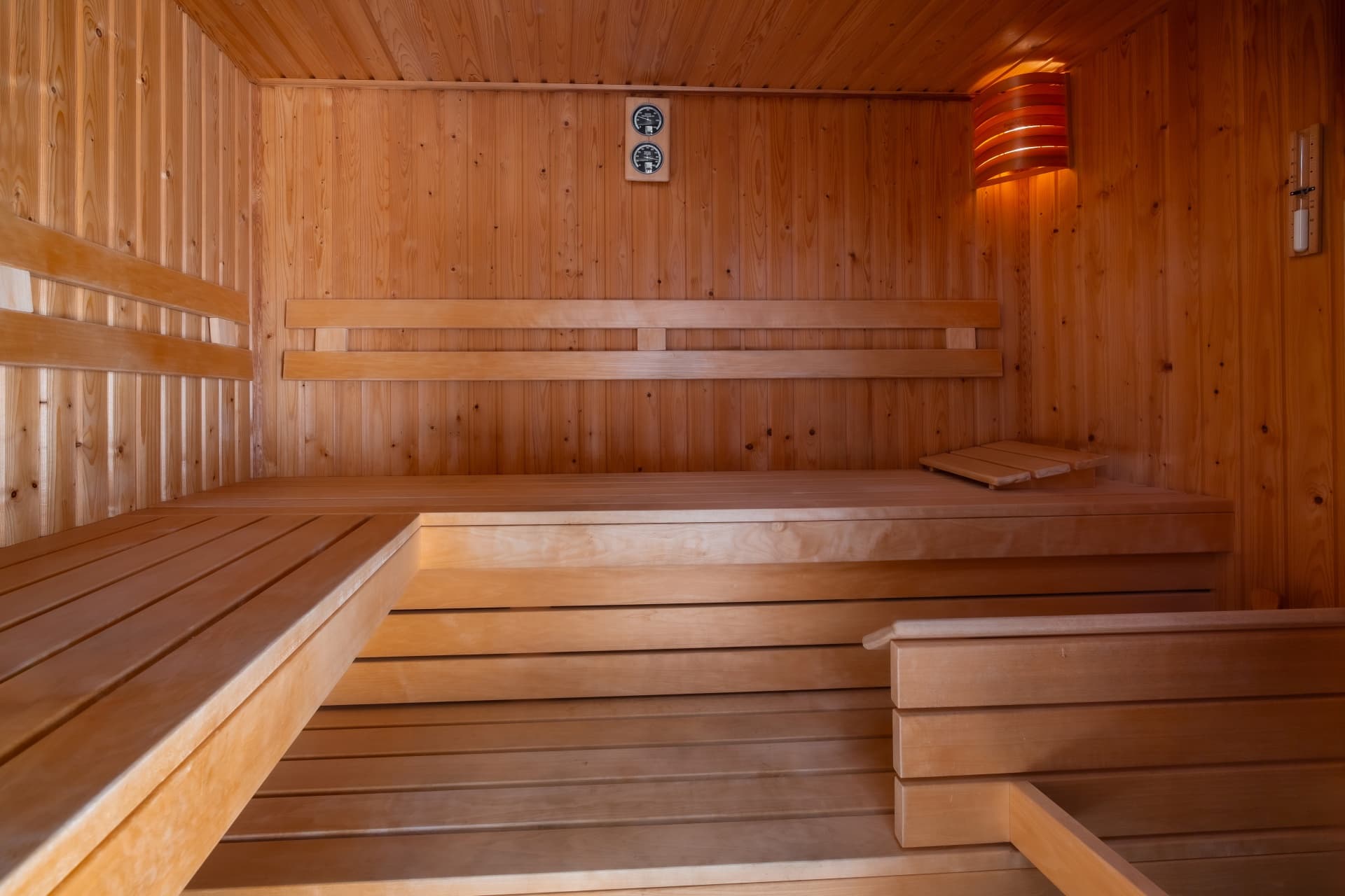 Leere Holzsauna mit mehrstufigen Sitzbänken, sanfter Beleuchtung und einem Thermometer an der Holzwand.